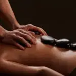 Massage therapist in Olympia, WA performing full body massage therapy on client comfortably positioned on a massage table with stones placed along their back in Olympia WA