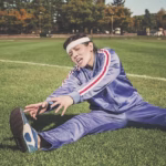 Woman in athletic clothing stretching near track and field area, representing athletic recovery and the benefits of sports massage therapy